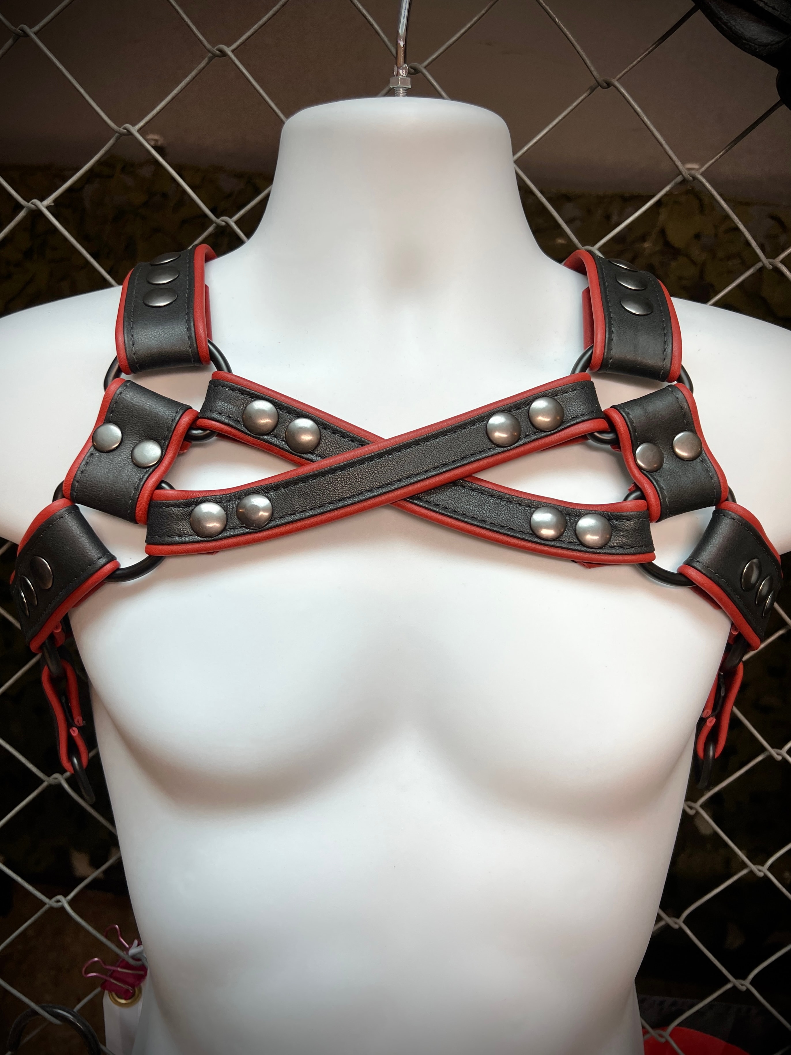 Black leather harness with red trim and studs on mannequin