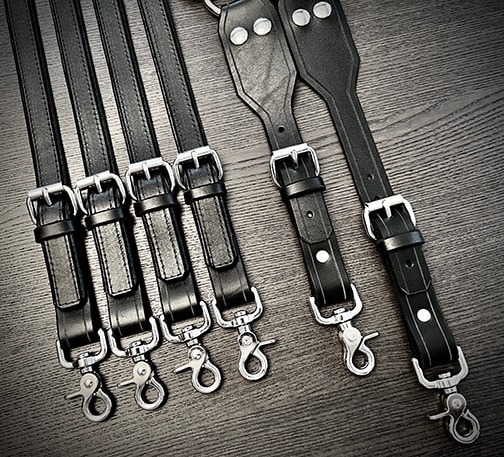 Black leather straps with snap hooks flat lay on dark wood